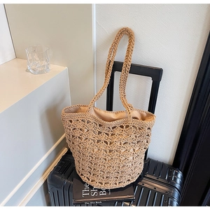Close-up of handmade straw bucket bag with hollow floral weave on a travel suitcase