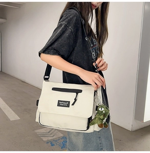 Detailed view of a white canvas messenger bag featuring a green dinosaur plush keychain charm