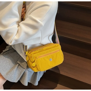 Detail of yellow nylon crossbody bag with multi-zipper pockets and purple strap