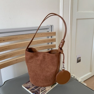 Detail view of brown suede bucket bag with a round coin purse and decorative knotted strap