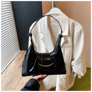 Détail du sac en cuir verni noir avec bande métallique dorée et bandoulière chic
