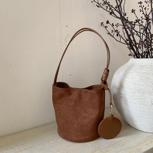 Detail view of a dark brown suede bucket bag with knotted shoulder strap on stone surface