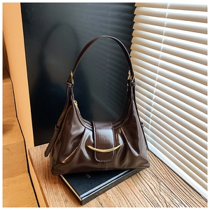 Détail du sac à bandoulière en cuir verni marron foncé avec boucle dorée en croissant sur livres