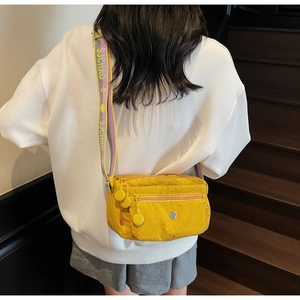 Detail view of yellow nylon crossbody bag with multi-pocket zippers and woven shoulder strap