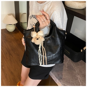 Detail of black croc-embossed tote bag with cute plush bear and bow charm accessory