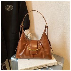 Sac demi-lune marron brillant avec plis vintage et boucle dorée sur une valise