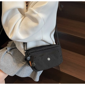 Detailed view of black nylon crossbody bag with multiple zippers and orange tag detail