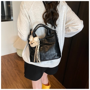 Close-up of black crocodile pattern handbag with plush bear charm worn by a model