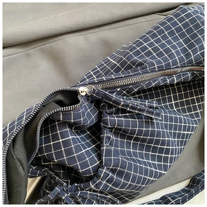 Detailed macro view of the silver metal zipper and blue plaid fabric texture of the bag