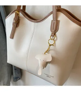 Detail of cream tote bag featuring brown leather trim and a cute elephant charm