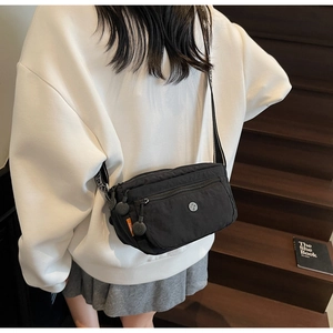 Detail of black nylon crossbody bag featuring multi-pocket design and wide patterned strap
