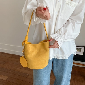 Detail of a bright yellow suede bucket bag featuring a unique knotted shoulder strap
