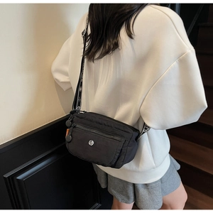 Close-up of black multi-pocket nylon crossbody bag with wide letter-print strap and metal logo