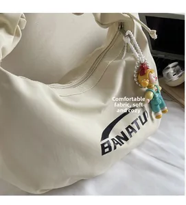 Détail du sac hobo en toile crème avec logo Banatu et pendentif poupée mignon