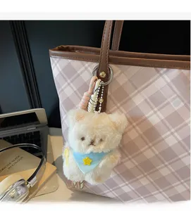 Gros plan d'un ours en peluche avec écharpe bleue accroché à un sac fourre-tout