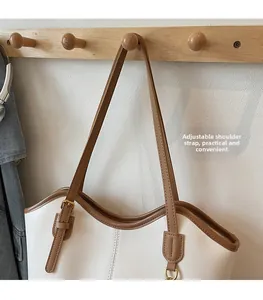 Detail of minimalist cream tote bag with adjustable brown leather strap on a wood hook