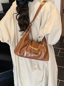Sac bandoulière en cuir marron avec boucle dorée, porté par un mannequin en intérieur