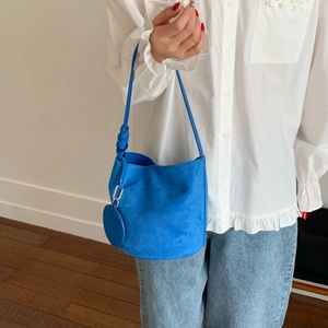 Detail of blue suede bucket bag with stylish knotted strap and small round charm accessory