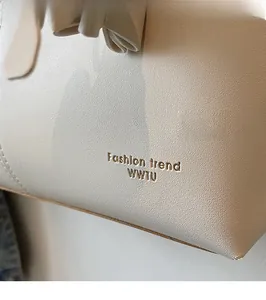 Close-up of cream textured faux leather handbag showing gold fashion trend lettering