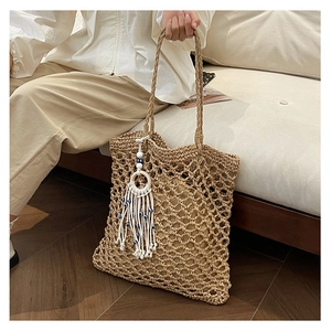 Detailed close-up of woven hollow mesh straw tote bag with decorative tassel and beads