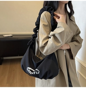 Détail d'un sac plissé noir avec logo blanc et bandoulière à volants moderne