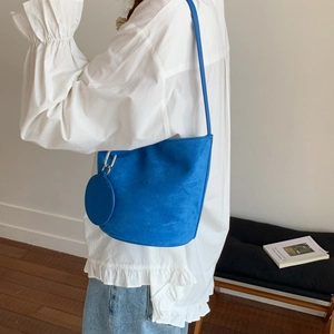 Detail of blue faux suede bucket bag with long strap and small round charm pendant