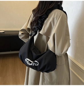 Détail d'un sac croissant plissé noir avec logo BANATU porté sur un trench-coat chic