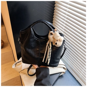 Detailed close-up of glossy black crocodile embossed faux leather handbag with cute bear charm
