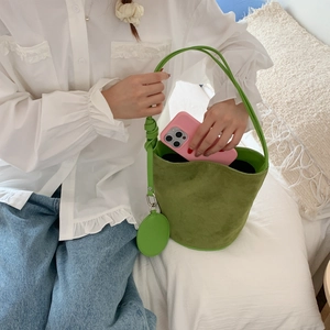 Detail shot of a matte green suede bucket bag with a matching coin purse on white bedding