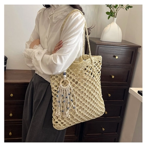 Detail of hand-woven straw tote bag with bohemian tassel charm and evil eye bead