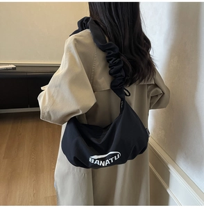 Détail de la bandoulière plissée et du logo blanc sur ce sac croissant noir en nylon