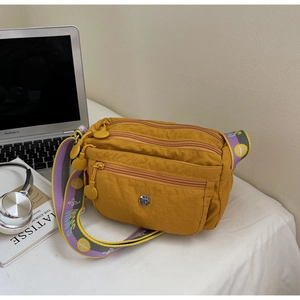 Detail view of mustard yellow nylon crossbody bag with multi-layer zippers and jacquard strap