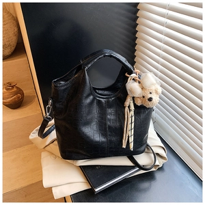Close-up of black crocodile pattern handbag with a cute plush bear pendant accessory