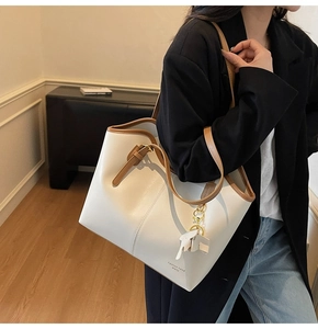 Side view of model wearing a large white and brown leather tote bag with an elephant charm