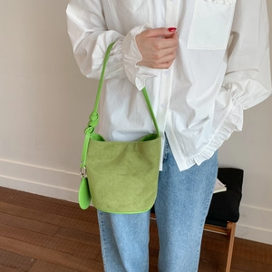 Detail of green suede bucket bag with knotted shoulder strap and circular charm