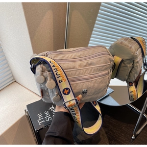 Detail view of light grey nylon crossbody bag with multiple zippers and wide woven strap