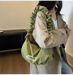 Détail du sac demi-lune vert avec bandoulière plissée et lettrage blanc BANAZA