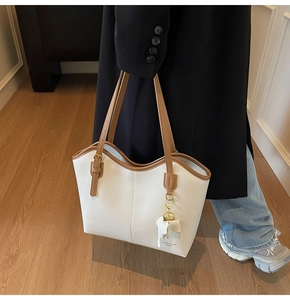 Detail of white tote bag with brown leather straps and elephant charm hanging accessory