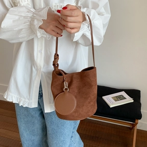 Detail of a brown suede bucket bag featuring a matching round coin purse charm and slim strap