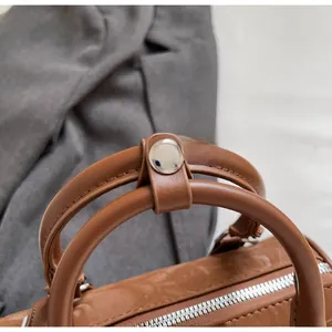 Detailed close-up of brown leather cylinder bag with silver metal zipper and round handle