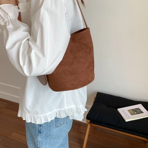 Brown suede bucket bag styled with a white ruffled shirt and light blue denim jeans