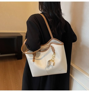 Close-up of a large beige tote bag with brown trim and a golden chain bow charm