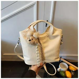 Detail of a beige crocodile pattern bucket bag with a cute bear charm and shoulder strap
