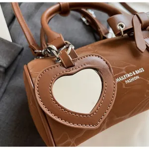 Detail of caramel brown cylinder bag with bow and heart mirror pendant accessory