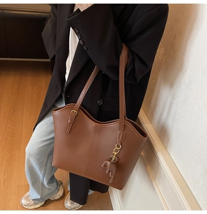 Detail of a brown matte leather tote bag with metallic buckle strap and leaf charm