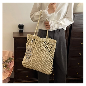 Detail of hand-woven straw tote bag with mesh pattern and blue beaded tassel charm