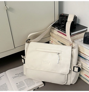Detail of cream messenger bag showing canvas texture, leather label, and buckle strap