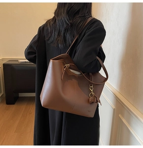 Detail of a brown leather tote bag with gold logo and a small elephant charm