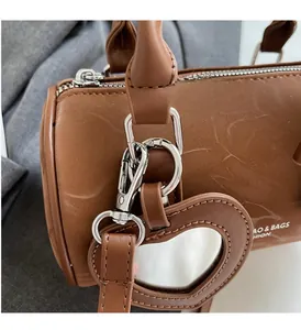 Close-up of brown cylinder bag showing silver zipper, metal hooks and heart mirror charm