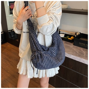 Blue and white plaid crescent bag with drawstring detail shown on a model's shoulder